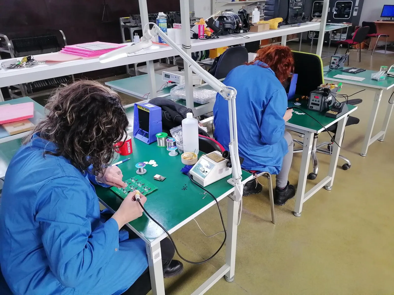 Двајца техничари на Velbit на ESD-безбедни работни маси, при рачно лемење и проверка на монтирани плочки.